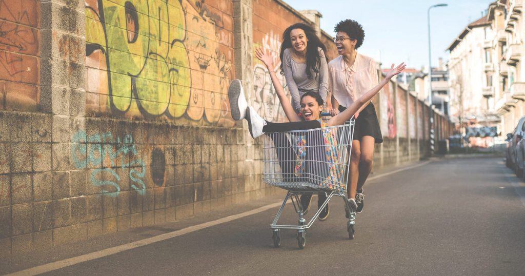 2 women pushing woman in shopping trolley